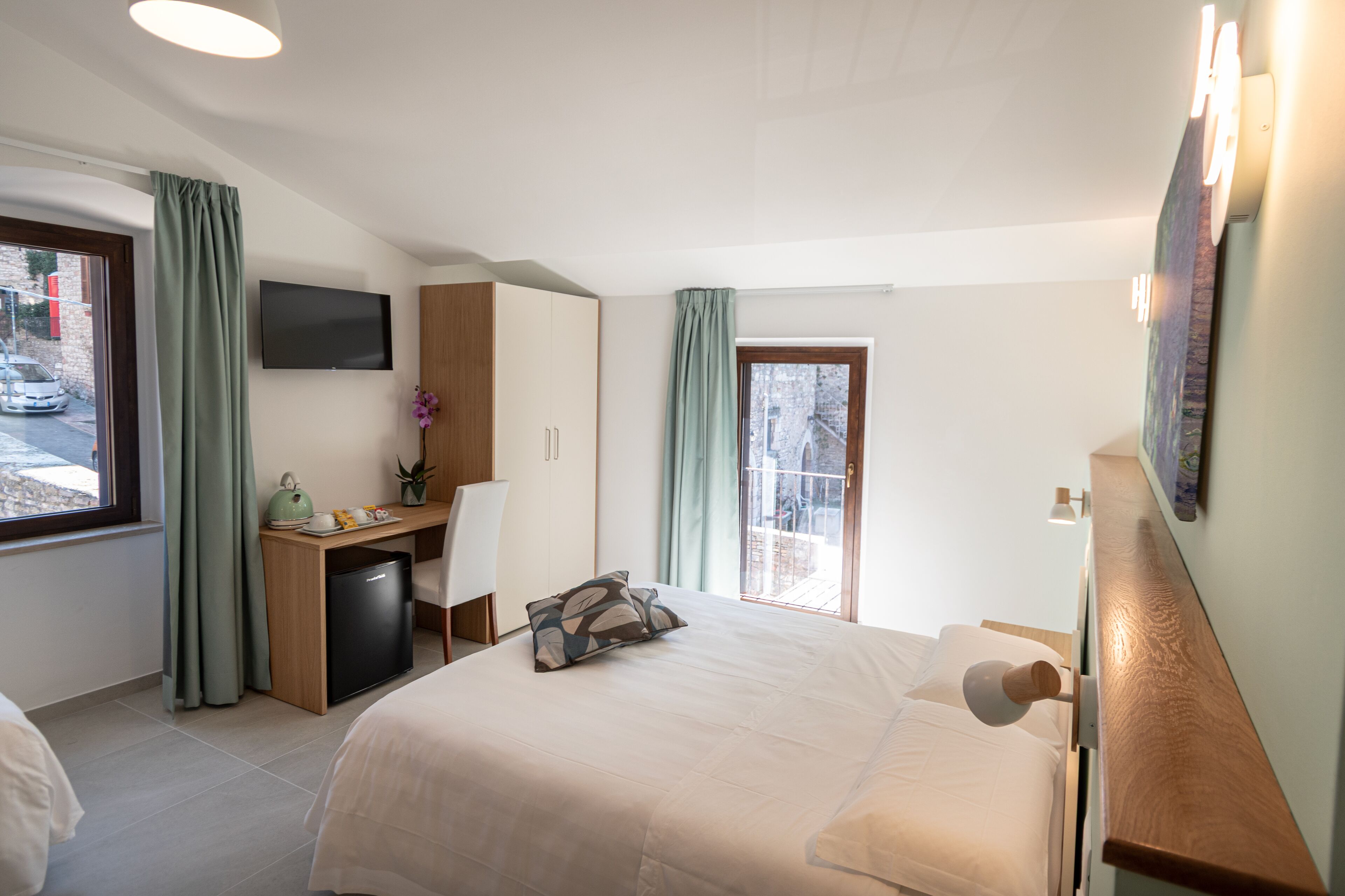 A hotel room with a bed, desk, chair, and a TV on the wall.