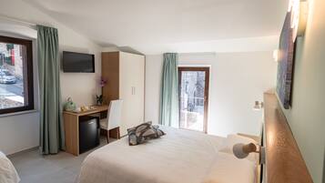 A hotel room with a bed, desk, chair, and a TV on the wall.