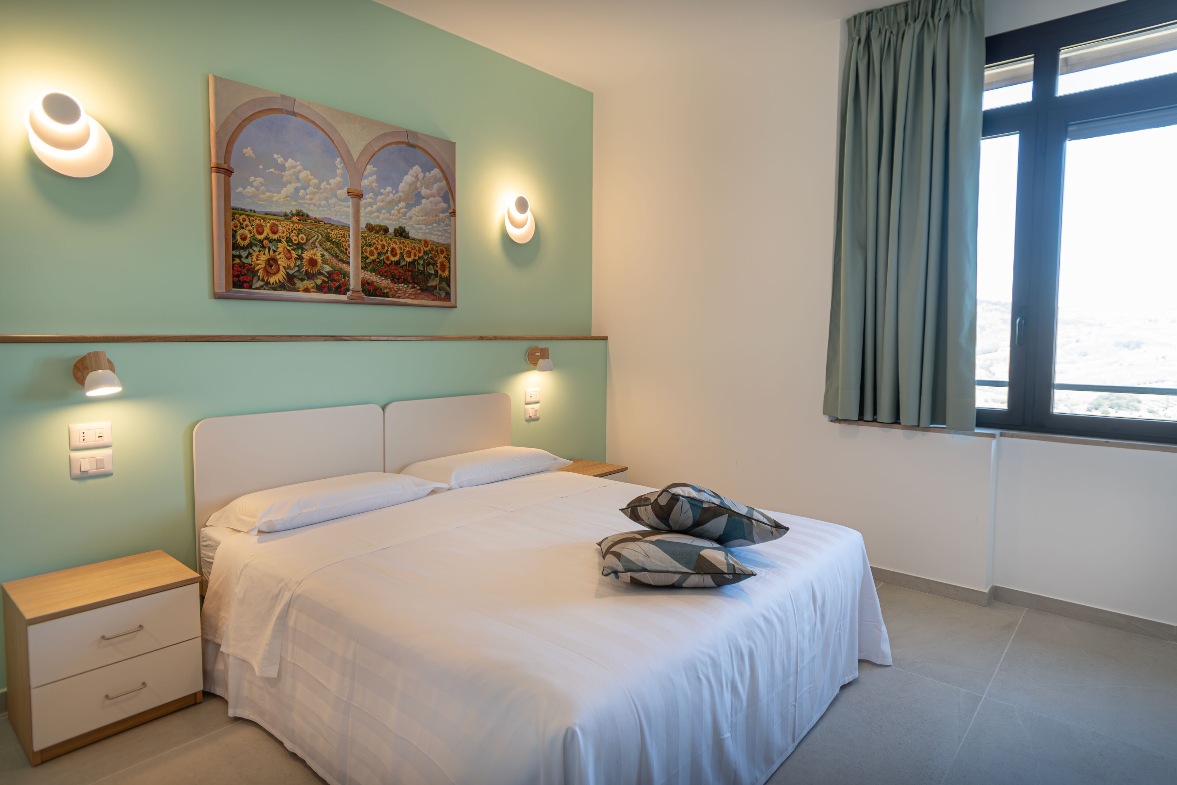 A bedroom with a bed, nightstands, wall sconces, and a painting.