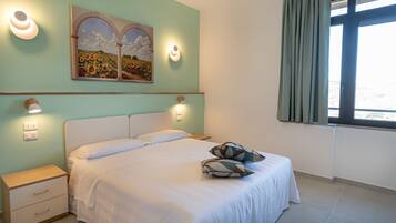 A bedroom with a bed, nightstands, wall sconces, and a painting.