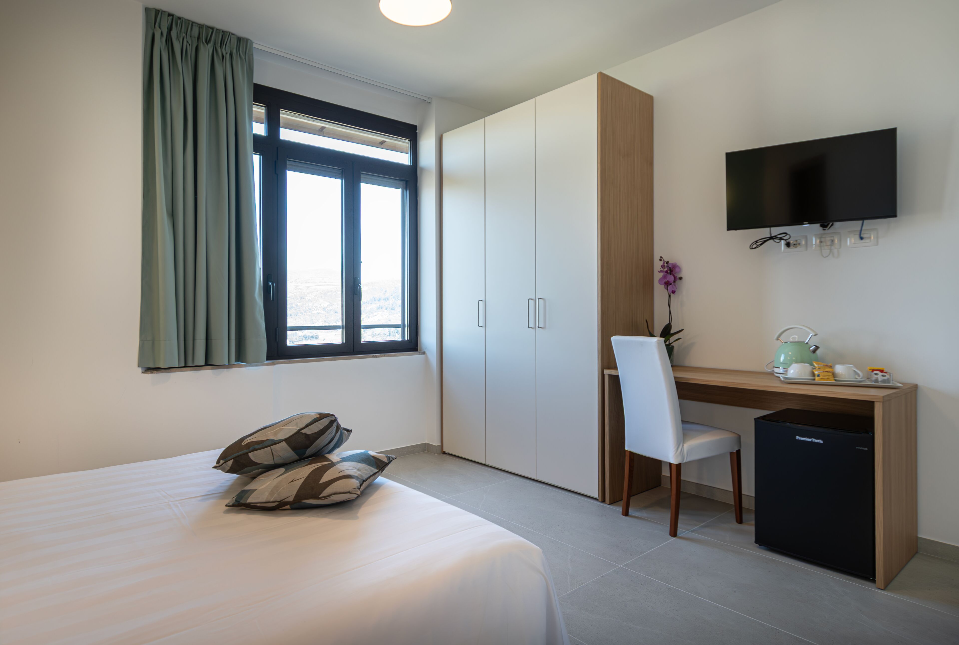 Ein Schlafzimmer mit einem Bett, einem Schreibtisch, einem Sessel, einem Fernseher und einem kleinen Kühlschrank.