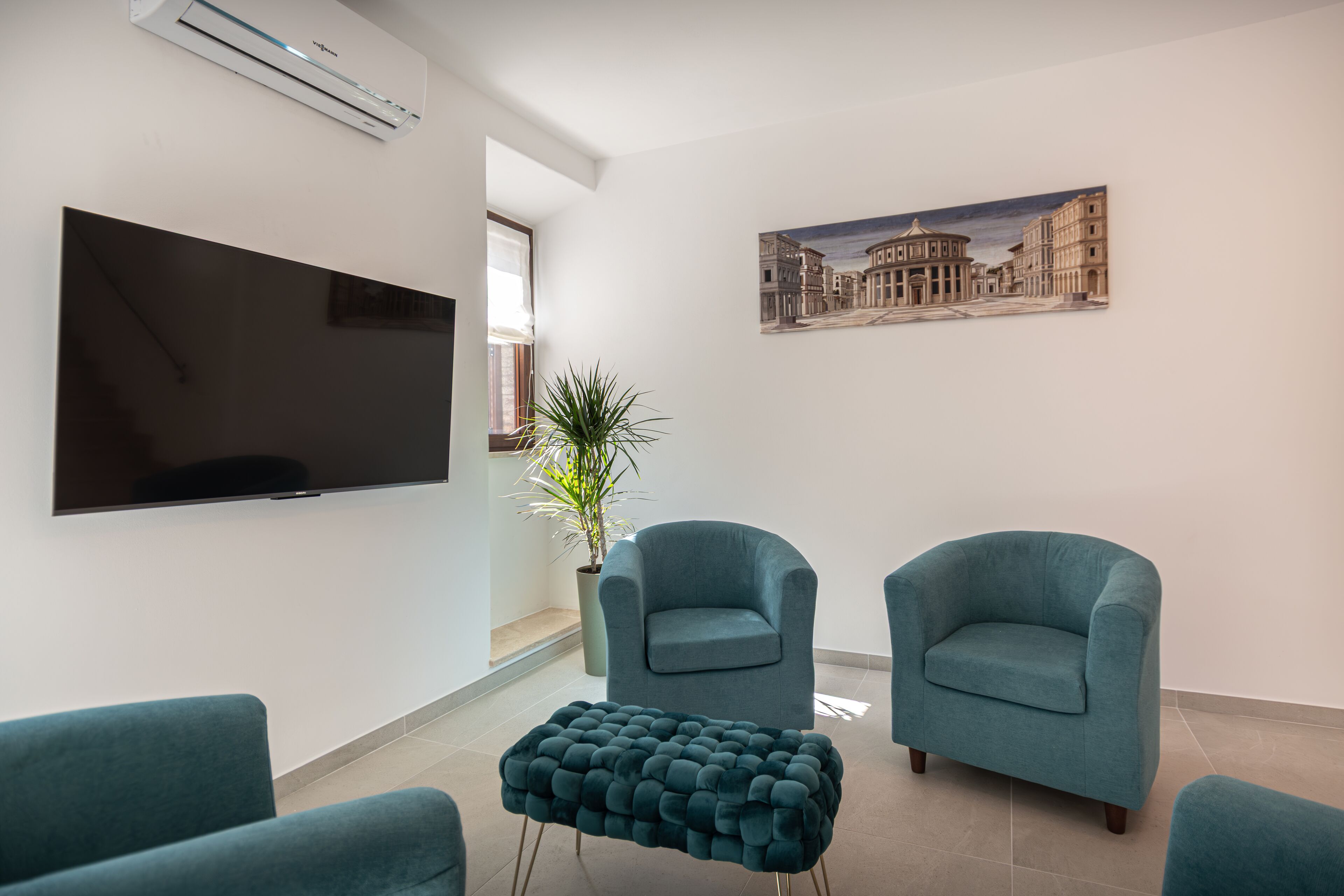 A modern living room with a flat-screen TV, two armchairs, a tufted ottoman, a potted plant, and a cityscape painting on the wall.
