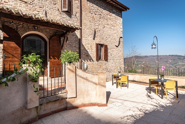 Un edificio de piedra con terraza, mobiliario exterior y vistas al campo.