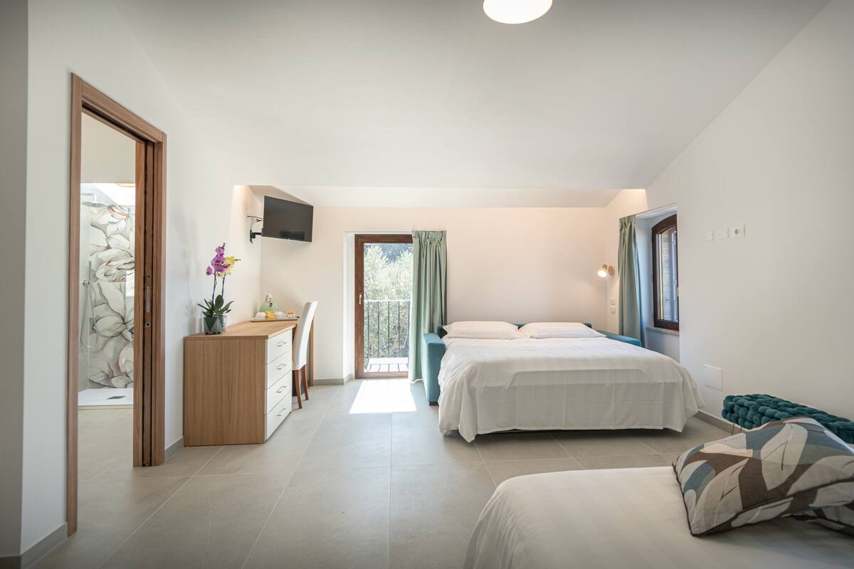 A bedroom with two beds, a desk, a TV, and a balcony.