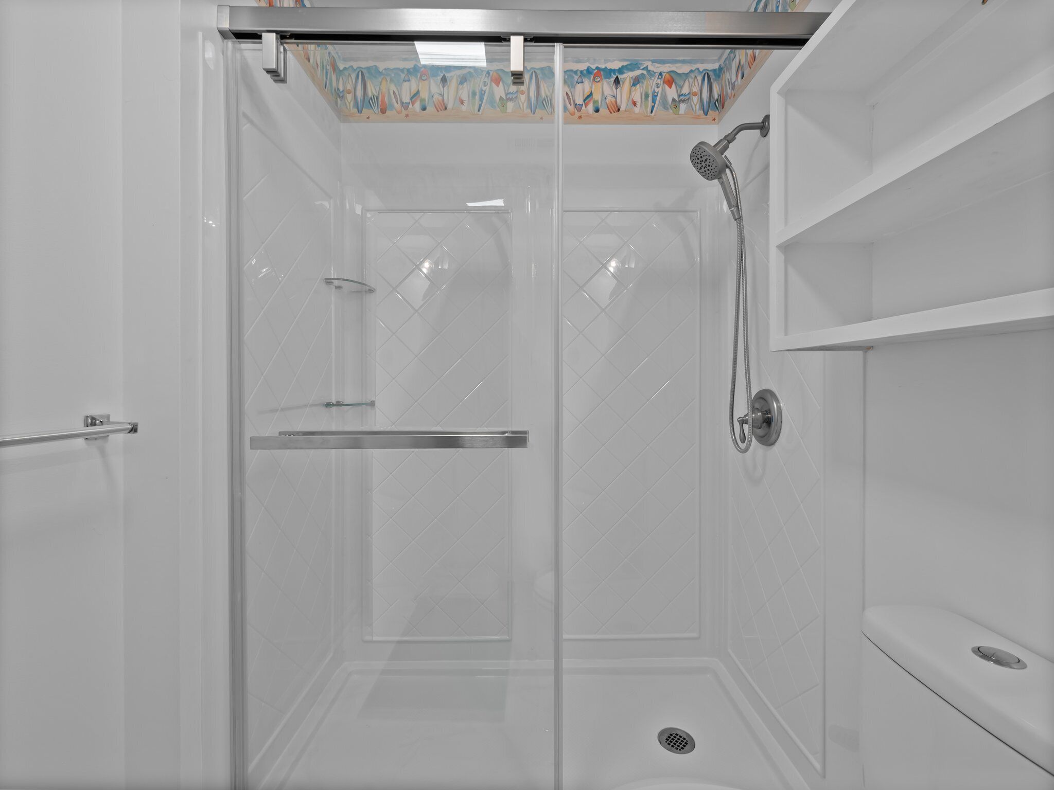 Ducha moderna con puerta de vidrio, cabezal de ducha de mano y pared de azulejos con un borde decorativo.