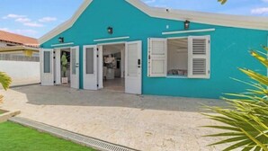 Un bâtiment turquoise avec des volets blancs, une entrée bien visible et une zone pavée devant.