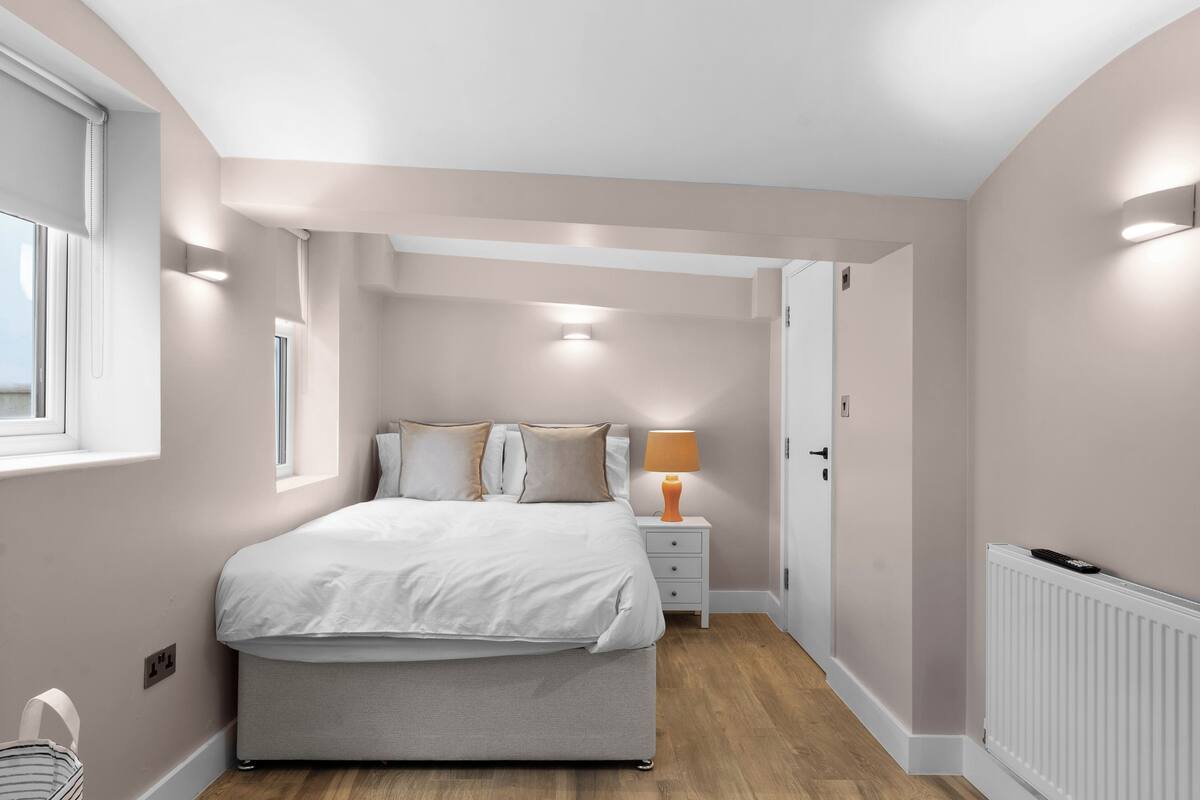 A bedroom with a bed, bedside table, lamp, and a window.