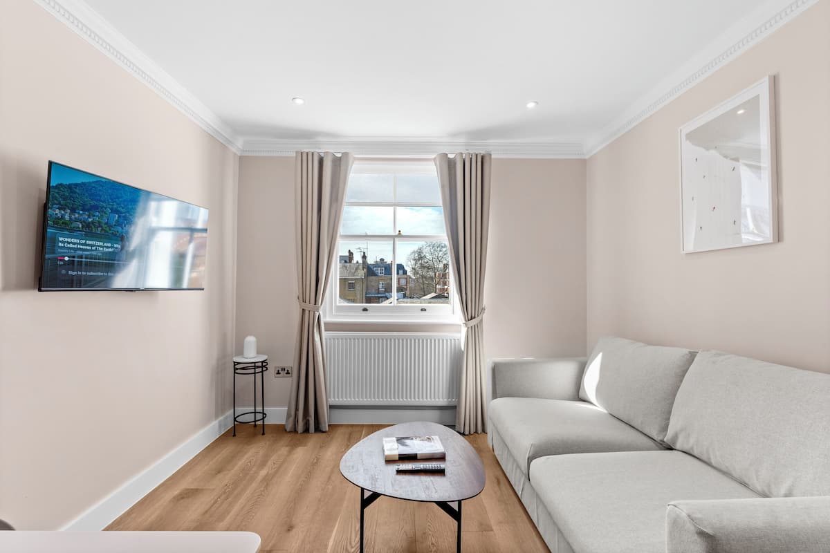 A modern living room with a sofa, a coffee table, a TV mounted on the wall, and a window with curtains.
