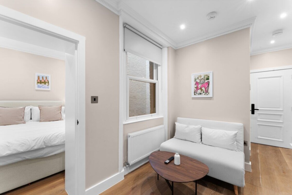 A modern hotel room with a bed, a sofa, a small table, a radiator, and a door.