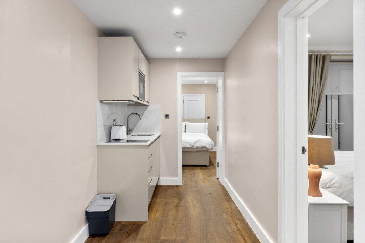 A narrow hallway with a kitchenette on the left, a bed in the center, and a bathroom on the right.