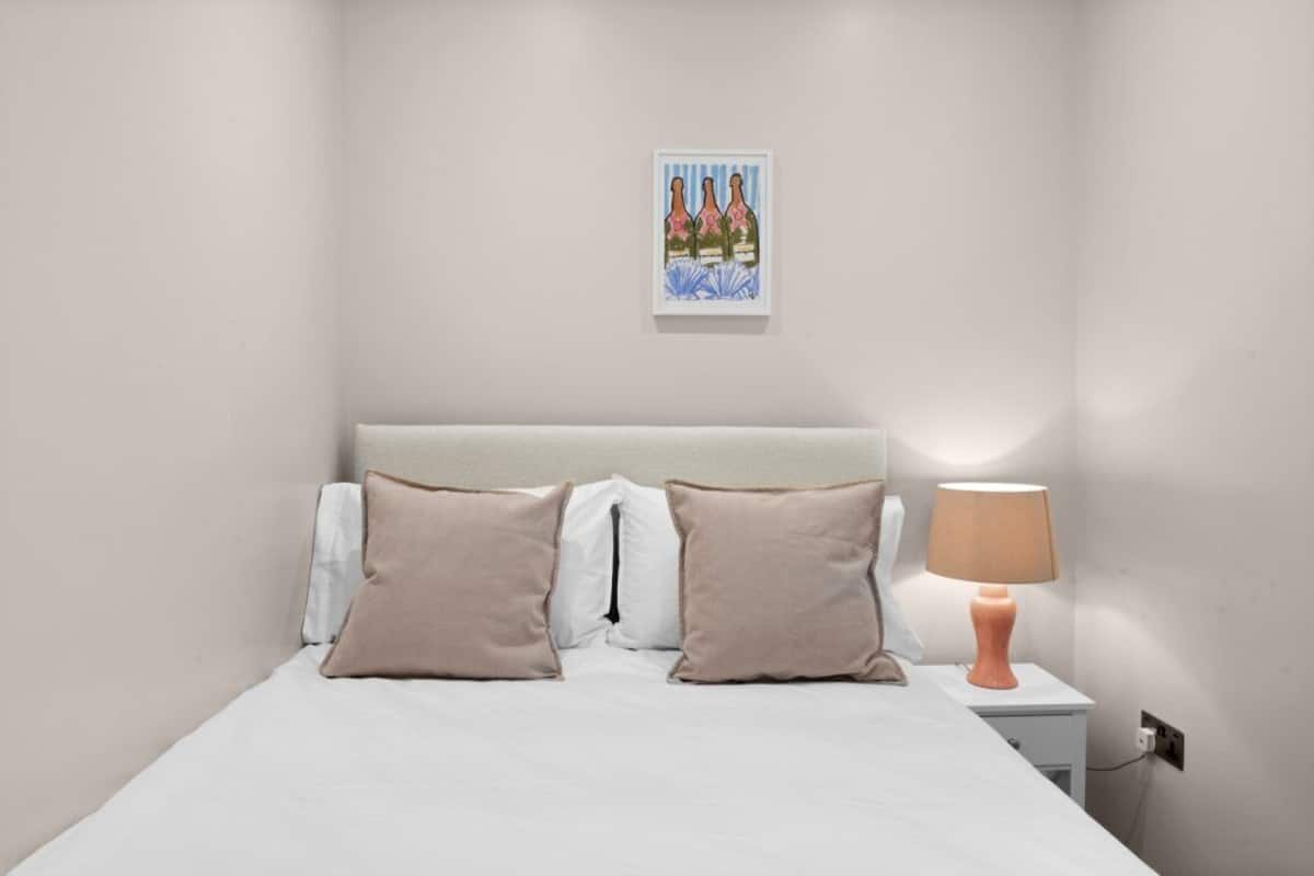 A bedroom with a bed, two pillows, a nightstand with a lamp, and a framed picture on the wall.
