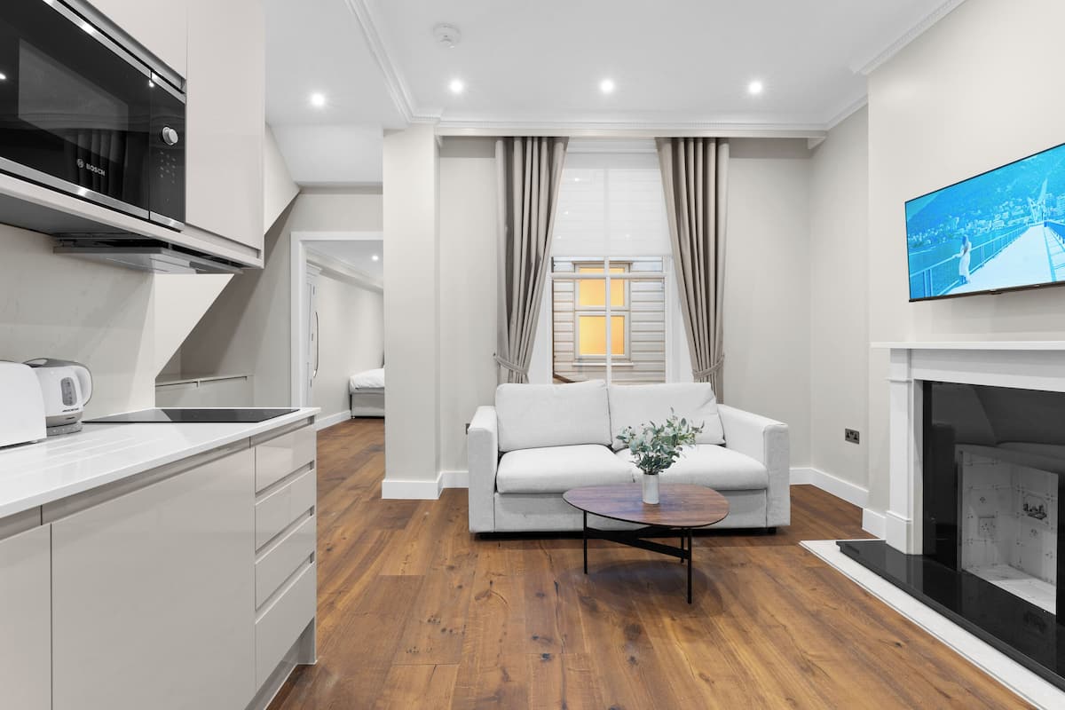 A modern kitchen with white cabinetry and a Bosch oven, a living area with a white sofa and a coffee table, and a fireplace.