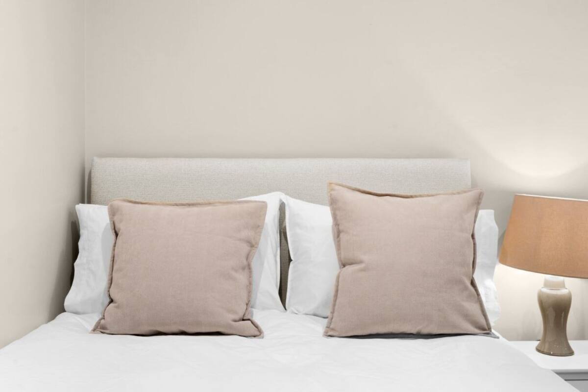 A bed with white and beige pillows, a headboard, and a bedside lamp.
