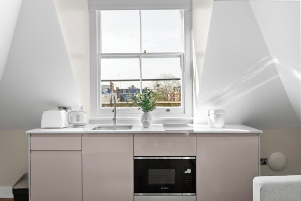 A modern kitchen with a Bosch microwave, a white countertop, a sink, and a window with a view of buildings. - Grove Heights Notting Hill (London)
