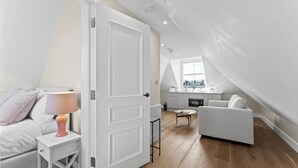 Ett modernt sovrum i loftstil med en säng, ett sängbord och en lampa. I bakgrunden syns ett litet kök med ett fönster ovanför.