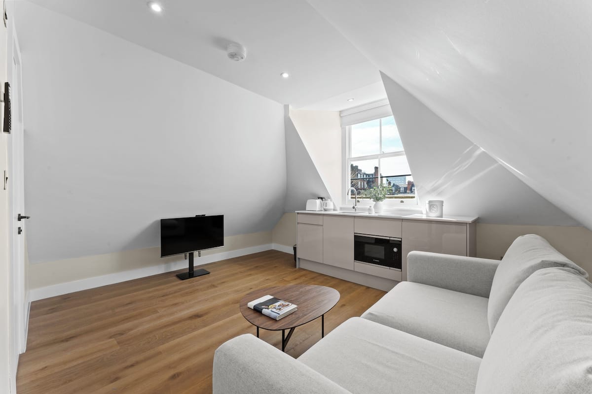 A modern apartment with a loft-style ceiling, a flat-screen TV, a small kitchen, and a sofa.
