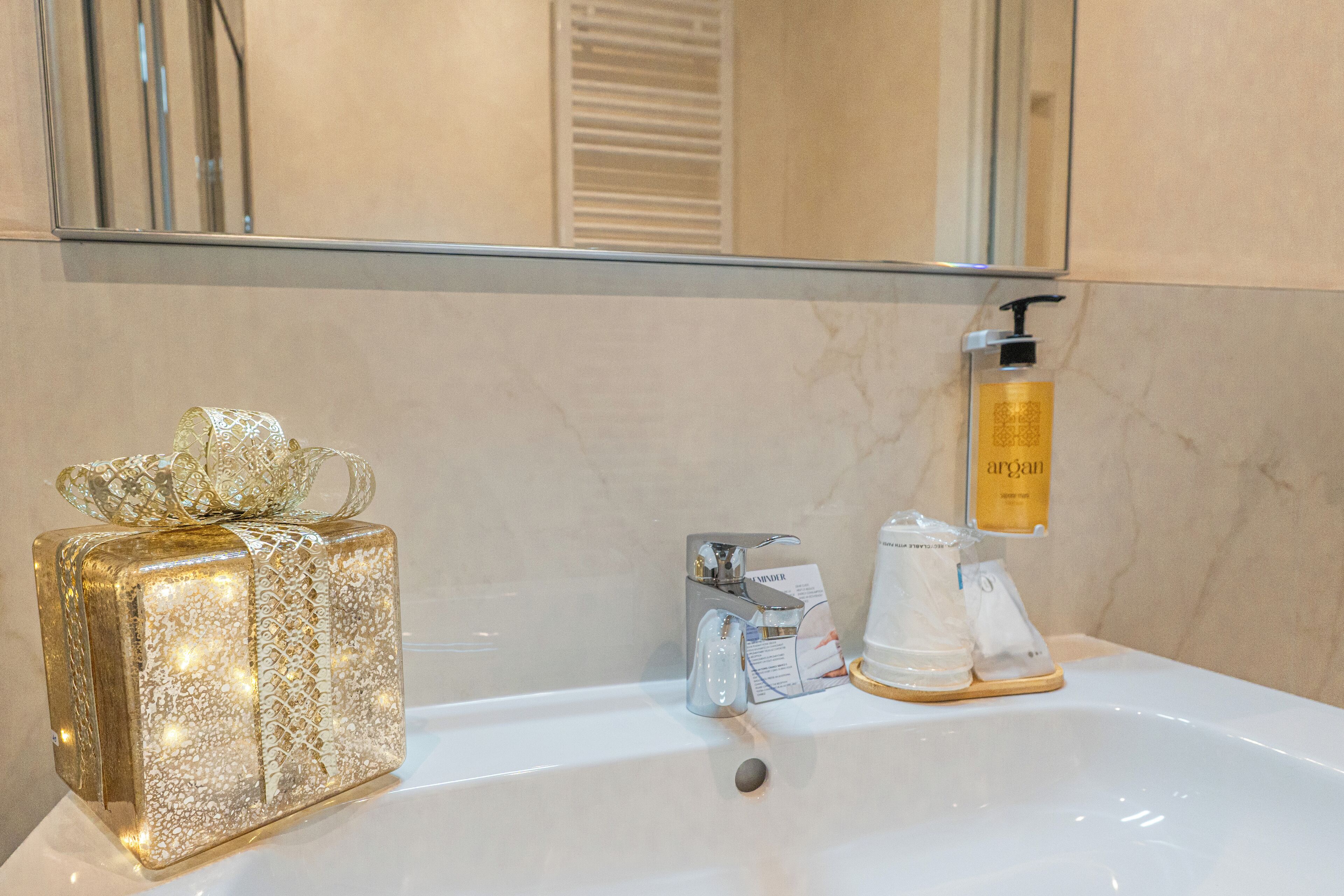 A bathroom with a white sink, a gift box, a bottle of Argan oil, and a mirror.