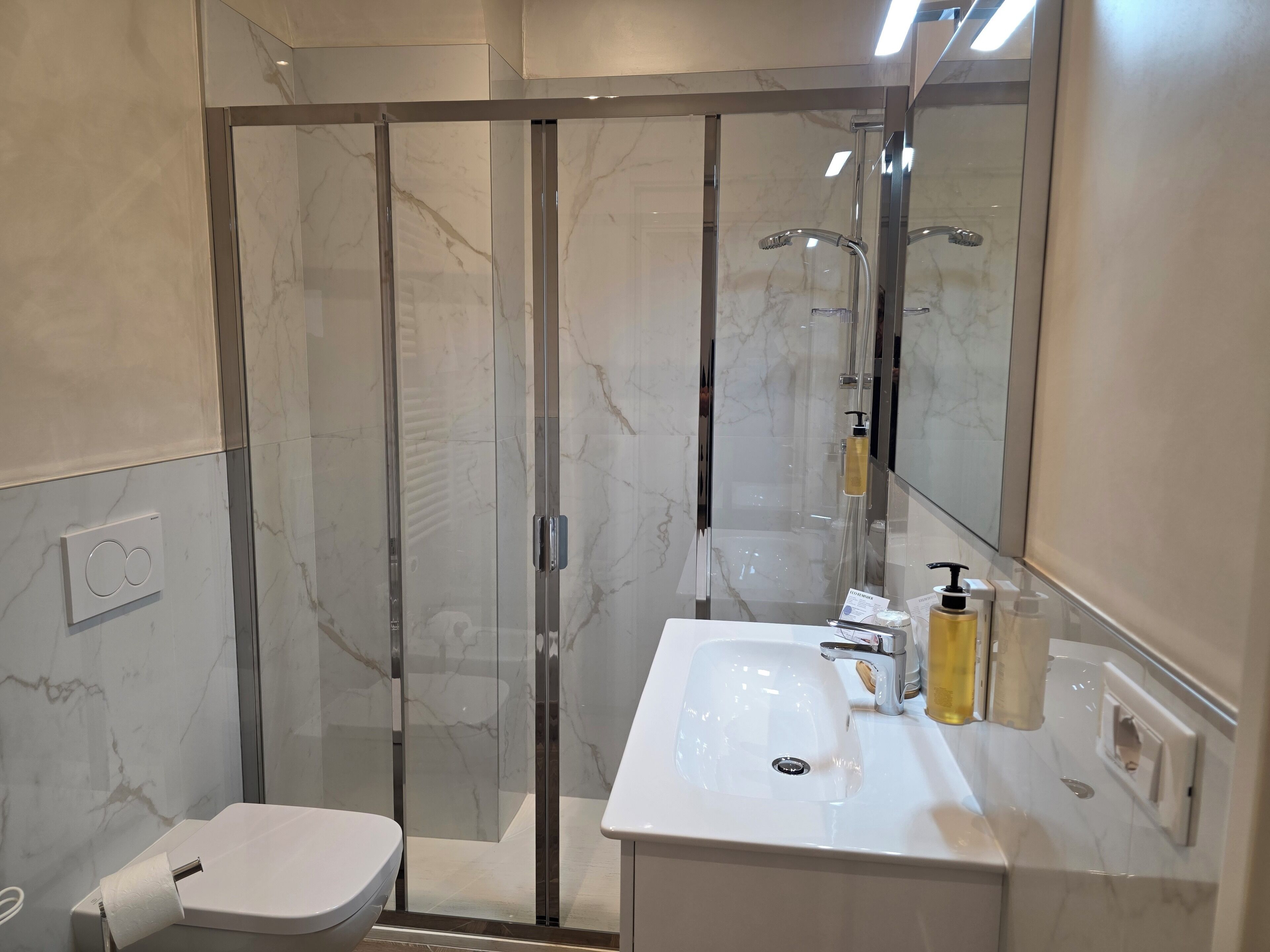 Un bany modern amb dutxa envidriada, un lavabo blanc amb mirall i productes de tocador a la superfície.