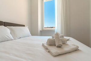 Una cama bien hecha con sábanas blancas y una ventana con cortinas.