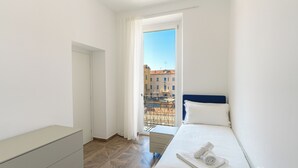 Une chambre d’hôtel moderne équipée d’un lit, d’une petite table de chevet, d’une armoire et d’un balcon offrant une vue sur les bâtiments.
