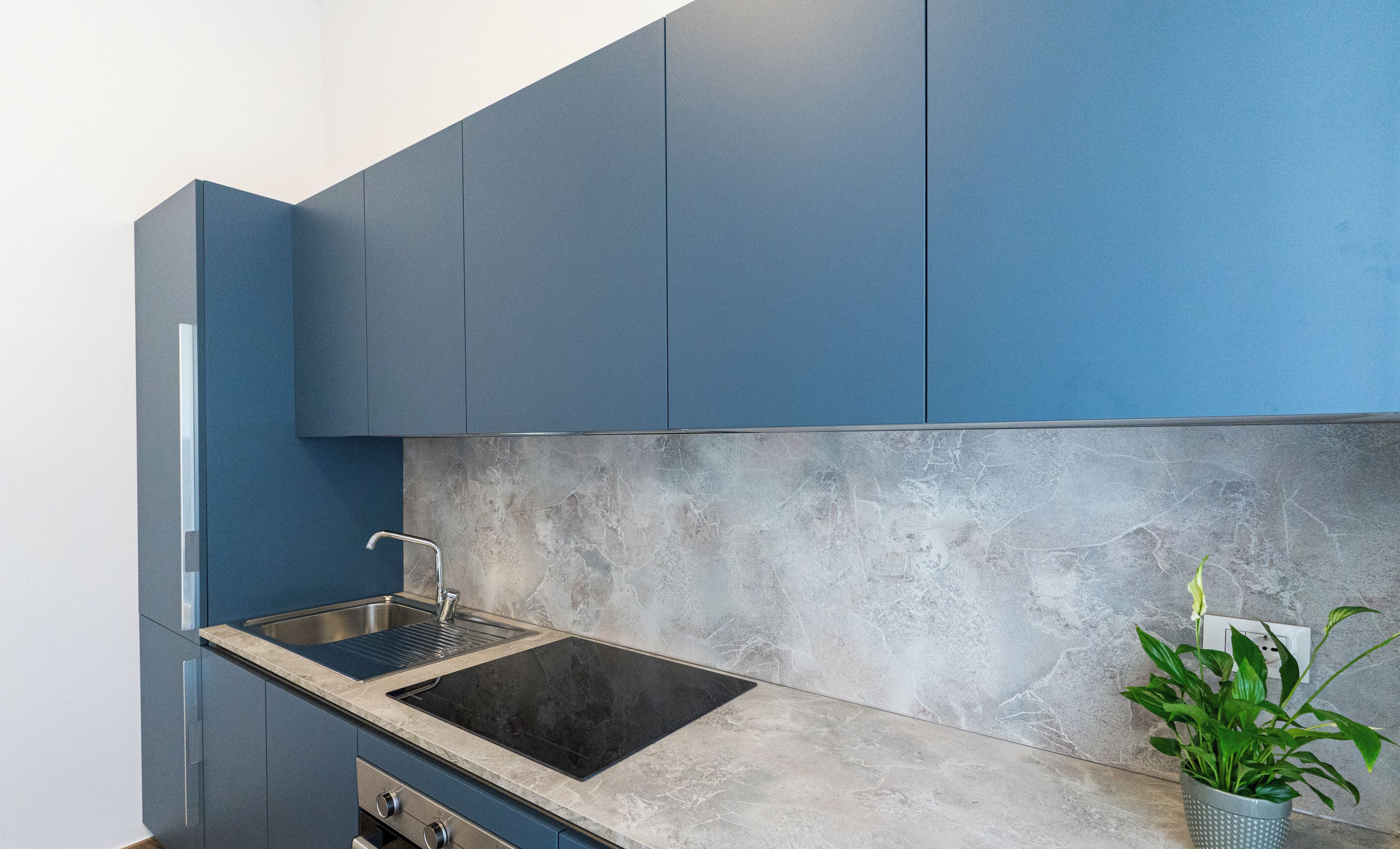 A modern kitchen with blue cabinets, a black stovetop, and a granite countertop.