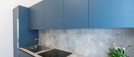 A modern kitchen with blue cabinets, a black stovetop, and a granite countertop.