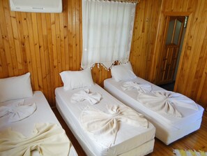 Een kamer met twee eenpersoonsbedden, elk voorzien van een witte deken en kussen. Er is een houten wand en een raam met een witte gordijn.