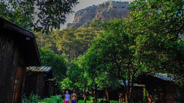 A narrow pathway flanked by wooden buildings with a mountainous backdrop. - Korsan Pansiyon (Kumluca)