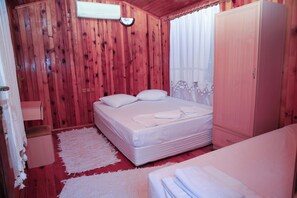 Un dormitorio con paredes de madera, una cama con ropa de cama blanca, un armario y una mesita de noche pequeña.