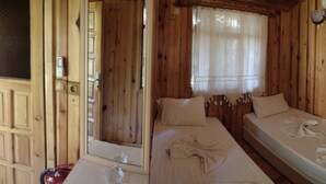 A wooden cabin room with two beds, a window with a curtain, and a door. - Korsan Pansiyon (Kumluca)