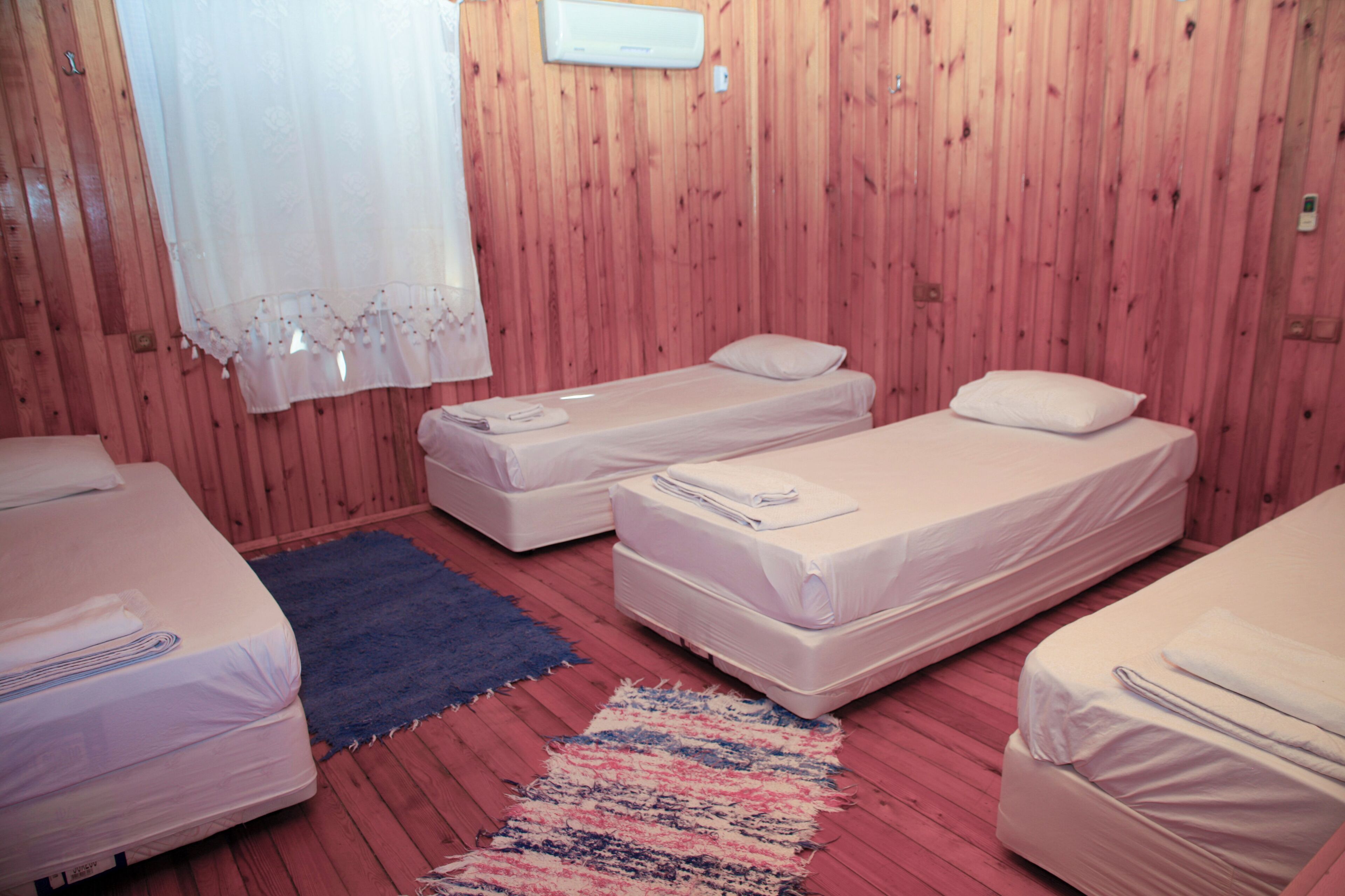 Quarto com duas camas de solteiro, um tapete azul e outro multicolorido, e paredes de madeira.