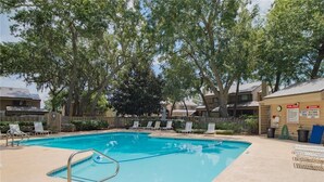A swimming pool with lounge chairs, a lifeguard stand, and a fenced area with trees. - Marsh 2 the Beach, 2 Bedroom Island Rental (Saint Simons Island)