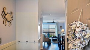 A hallway with a decorative crab wall art, a staircase, and a view to a balcony with outdoor seating. - Marsh 2 the Beach, 2 Bedroom Island Rental (Saint Simons Island)