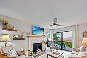 Un salon spacieux doté d’une cheminée, de sièges confortables, d’une télévision et d’un balcon offrant une vue sur la plage.