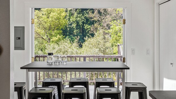 Un balcon avec une table et des chaises, une vue sur les arbres et une porte dotée d’une serrure.