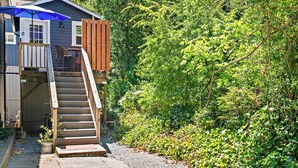 Une terrasse en bois avec un escalier menant à une maison surmontée d’un parasol bleu.