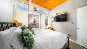 Un dormitorio con una cama grande, ventilador de techo, televisor montado y una puerta.