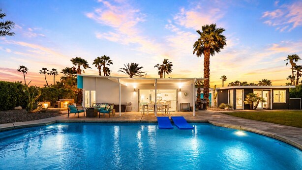 Una piscina con sillones de descanso, un patio techado y palmeras.