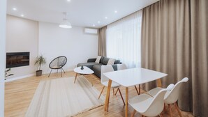 Una sala de estar moderna con un sofá, una mesa de comedor con sillas, una mesita auxiliar, una planta en maceta y un equipo de aire acondicionado de pared.