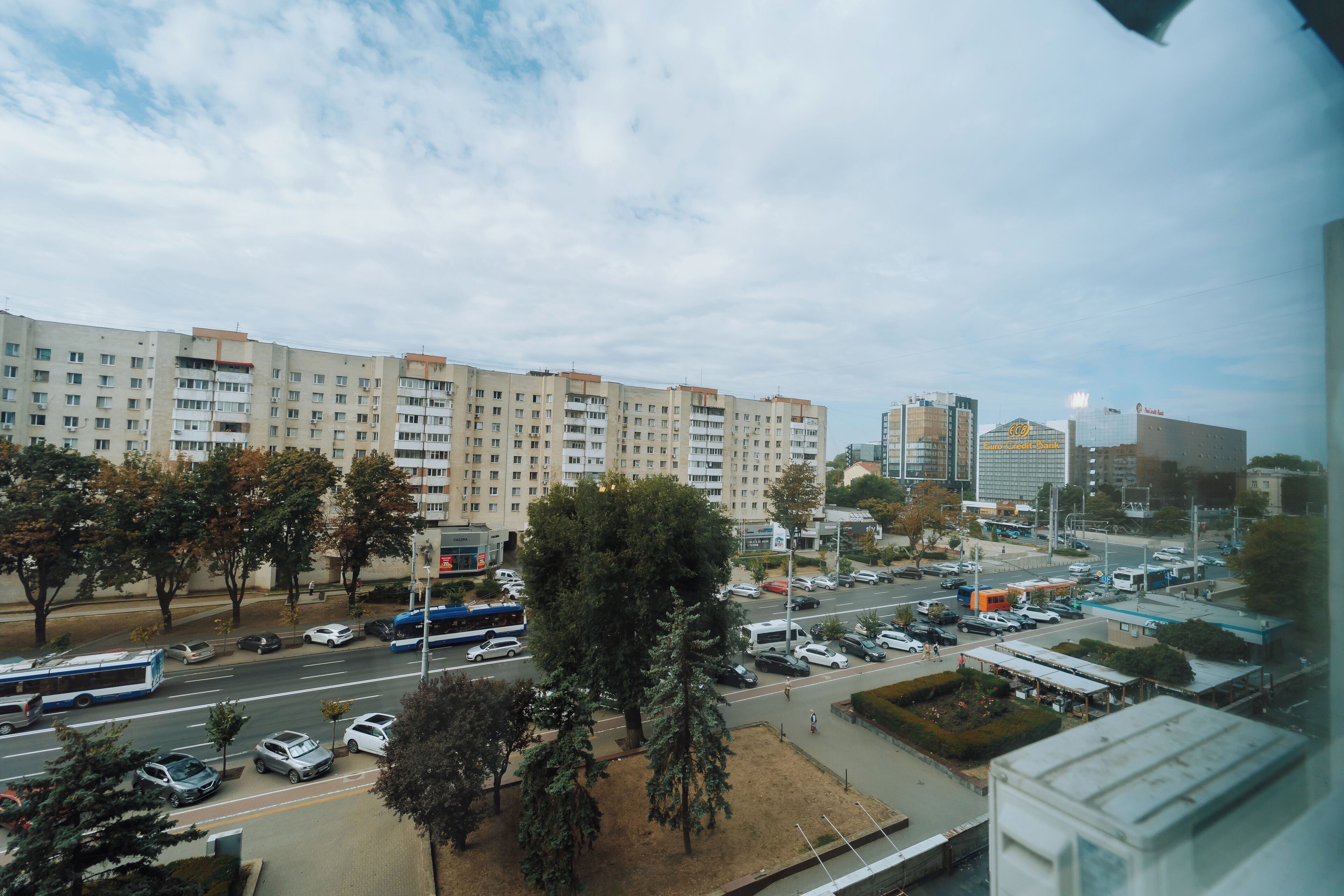 A cityscape with a large multi-story building, a parking lot, and a bus.