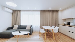 Una sala de estar moderna con un sofá gris, una mesita blanca y una zona de comedor con sillas blancas y una mesa de madera.