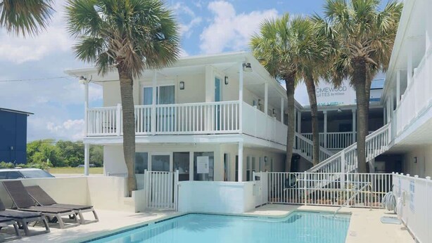 A two-story hotel with a swimming pool, white balconies, and palm trees. - Boutique on the beach, Studio #116 + Pool (Myrtle Beach)