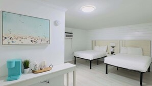 A hotel room with two beds, a white console table with a coffee maker, a painting of a beach scene, and a ceiling light. - Boutique on the beach, Studio #116 + Pool (Myrtle Beach)