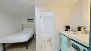 Une petite pièce propre, comprenant un lit, une salle de bain et une kitchenette.