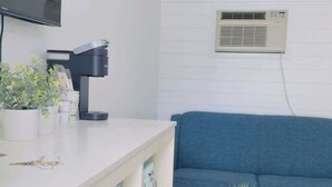 Ein modernes Wohnzimmer mit einem weißen Sofa, einem Couchtisch, einem an der Wand montierten Fernseher und einer Klimaanlage.