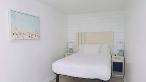 Ein Schlafzimmer mit einem Bett, zwei Nachttischen, einem Wandbild und einem Nachtschränkchen.