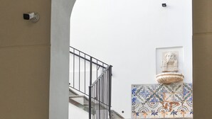 Un escalier avec une rampe noire, menant à un palier doté d’un mur recouvert de carreaux et d’une statue.