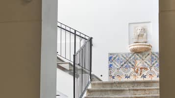 A staircase with a black railing, leading to a landing with a tiled wall and a statue.