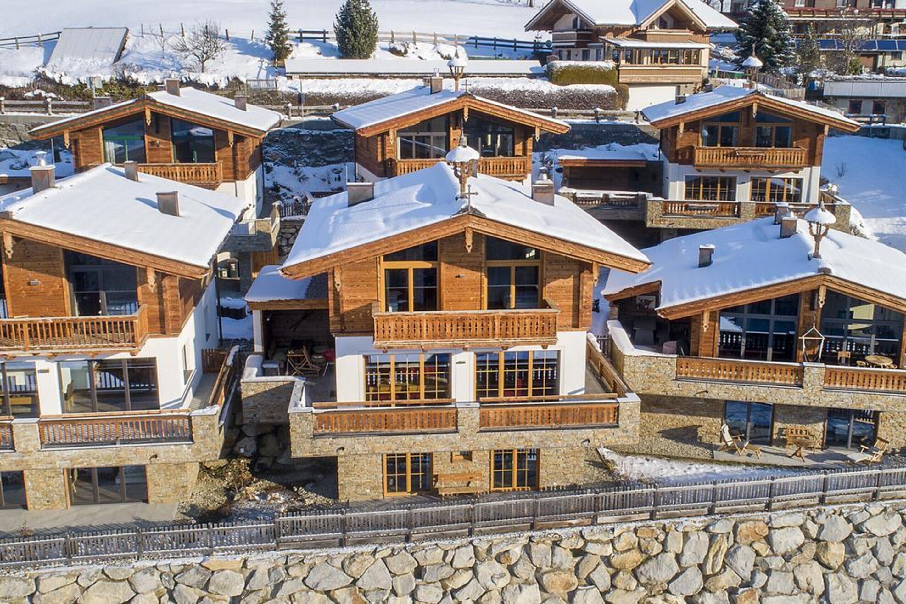 A cluster of chalet-style buildings with wooden balconies and stone foundations, surrounded by snow.