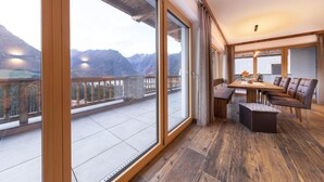 A spacious balcony with a wooden floor and glass doors, offering a view of mountains.